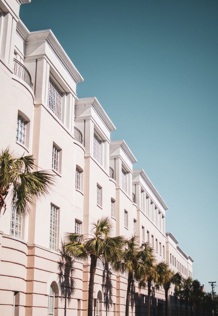 why-choose-us-02 Bright modern building facade with palm trees against a clear blue sky.