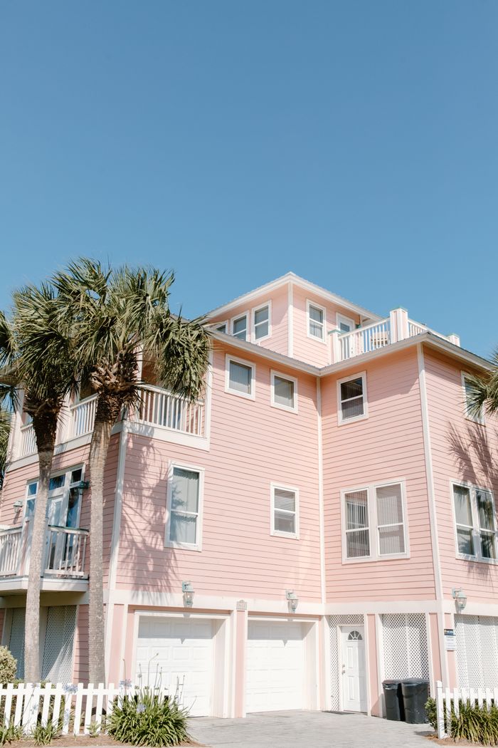 A pastel pink beach house with palm trees against a clear blue sky, perfect for coastal living themes.